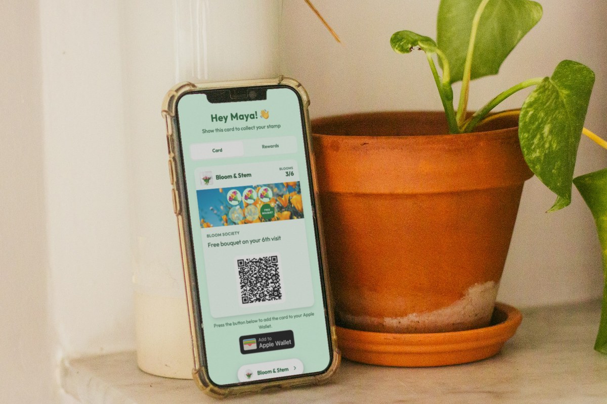 Illustration: a phone leans against a terracotta plant pot on a marble ledge, showing a Bloom & Stem florist loyalty card at 3 of 6 visits with the line 'Free bouquet on your 6th visit' and a QR code